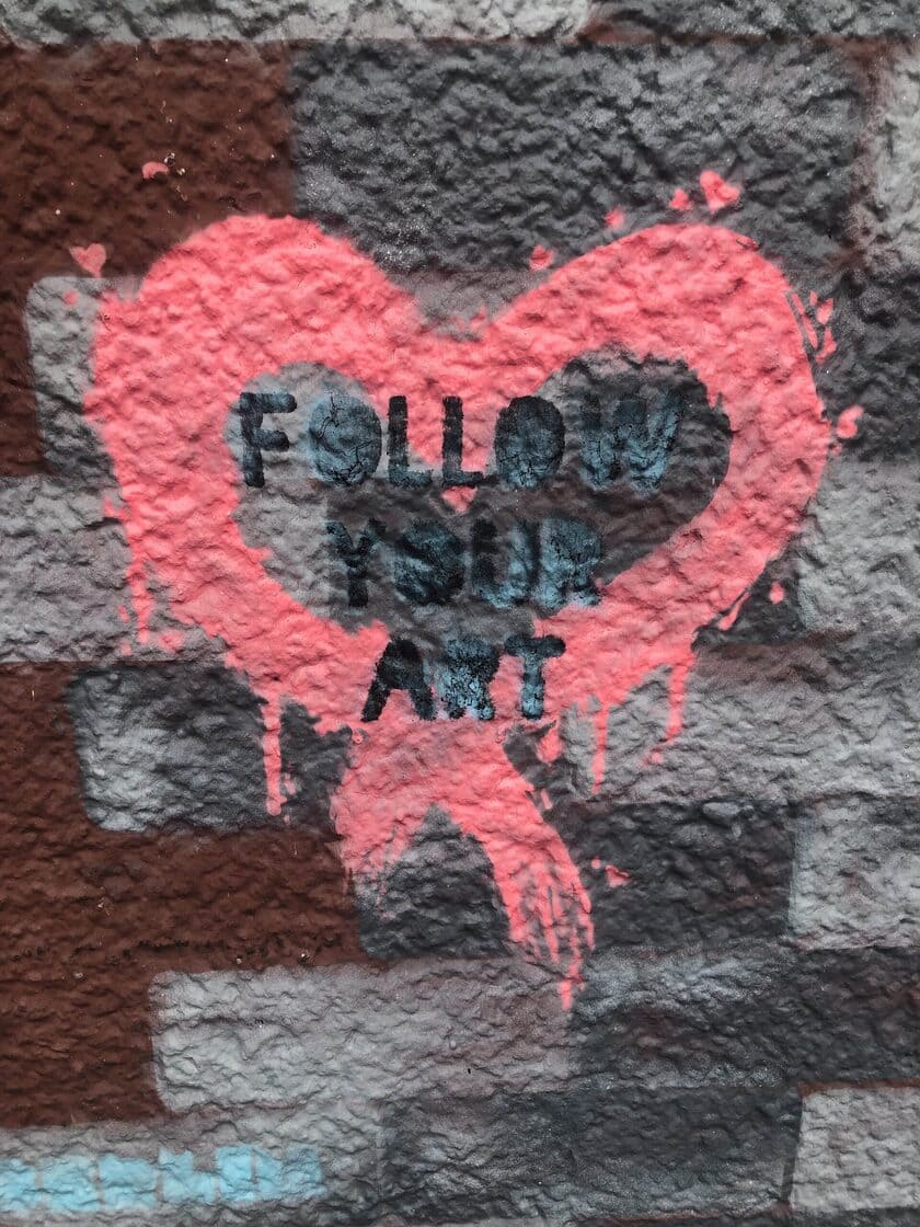 Corazón rosa pintado con aerosol con texto oscuro sobre muro texturizado.