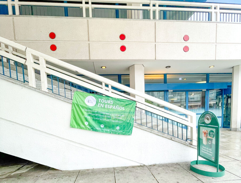 Cartel verde anunciando tours en español colgado en una rampa exterior junto a la entrada del Berliner Fernsehturm en Berlín, Alemania.